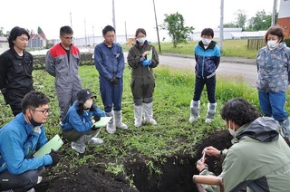 写真 土壌断面調査で普及指導員が土壌硬度の説明をする様子